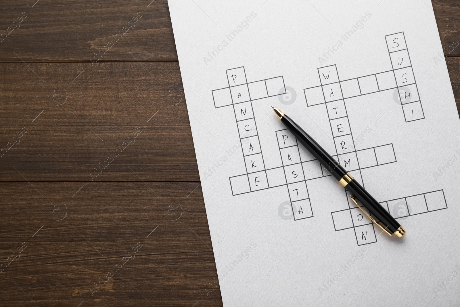 Photo of Crossword with answers and pen on wooden table, top view. Space for text