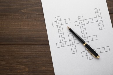 Crossword with answers and pen on wooden table, top view. Space for text