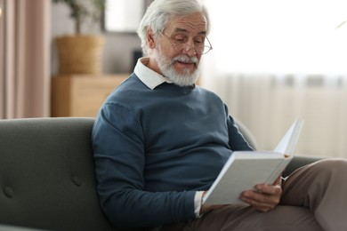 Photo of Portrait of happy grandpa reading book on sofa indoors