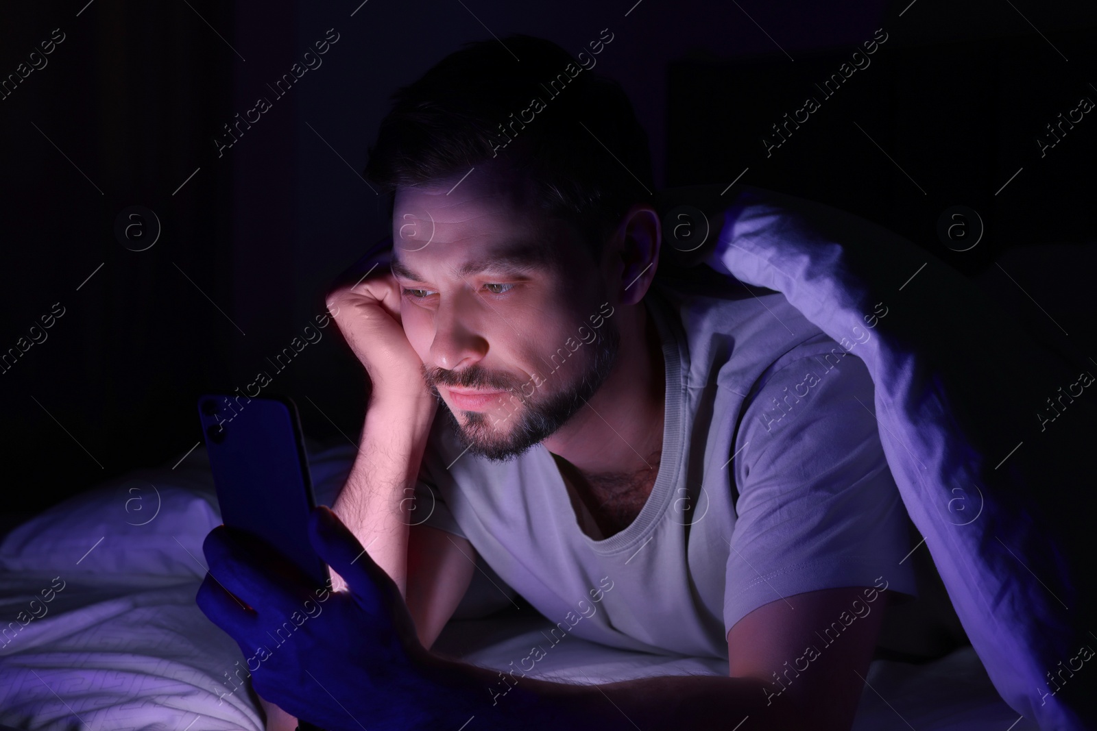 Photo of Man using smartphone in bed at night. Internet addiction