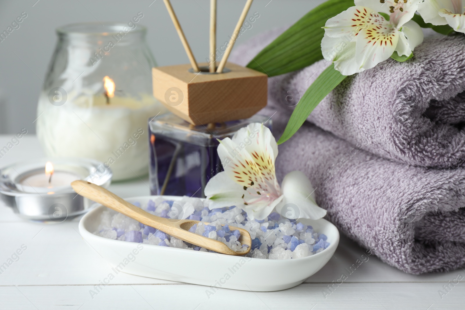 Photo of Spa composition. Towels, burning candles, reed air freshener, sea salt and beautiful flowers on white wooden table, closeup