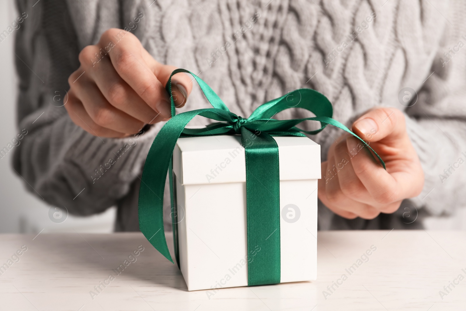 Photo of Woman decorating gift box at white table, closeup. Christmas present