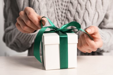 Photo of Woman decorating gift box at white table, closeup. Christmas present