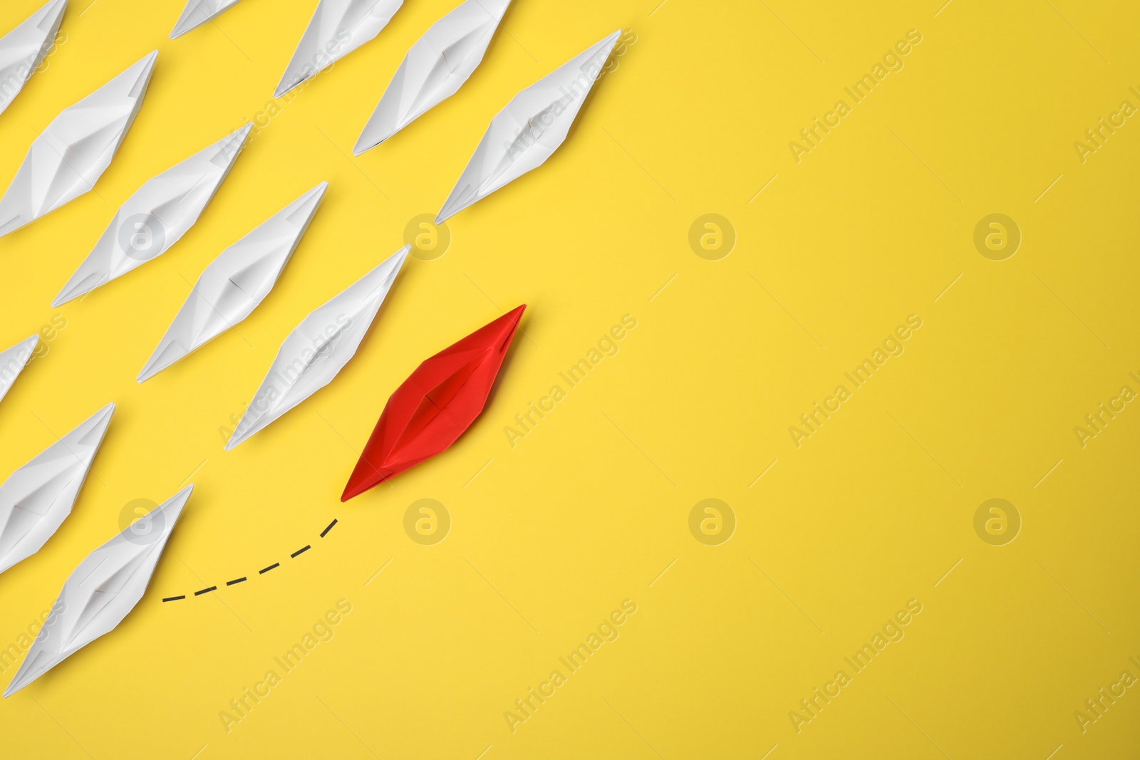 Photo of Red paper boat floating away from others on yellow background, flat lay with space for text. Uniqueness concept