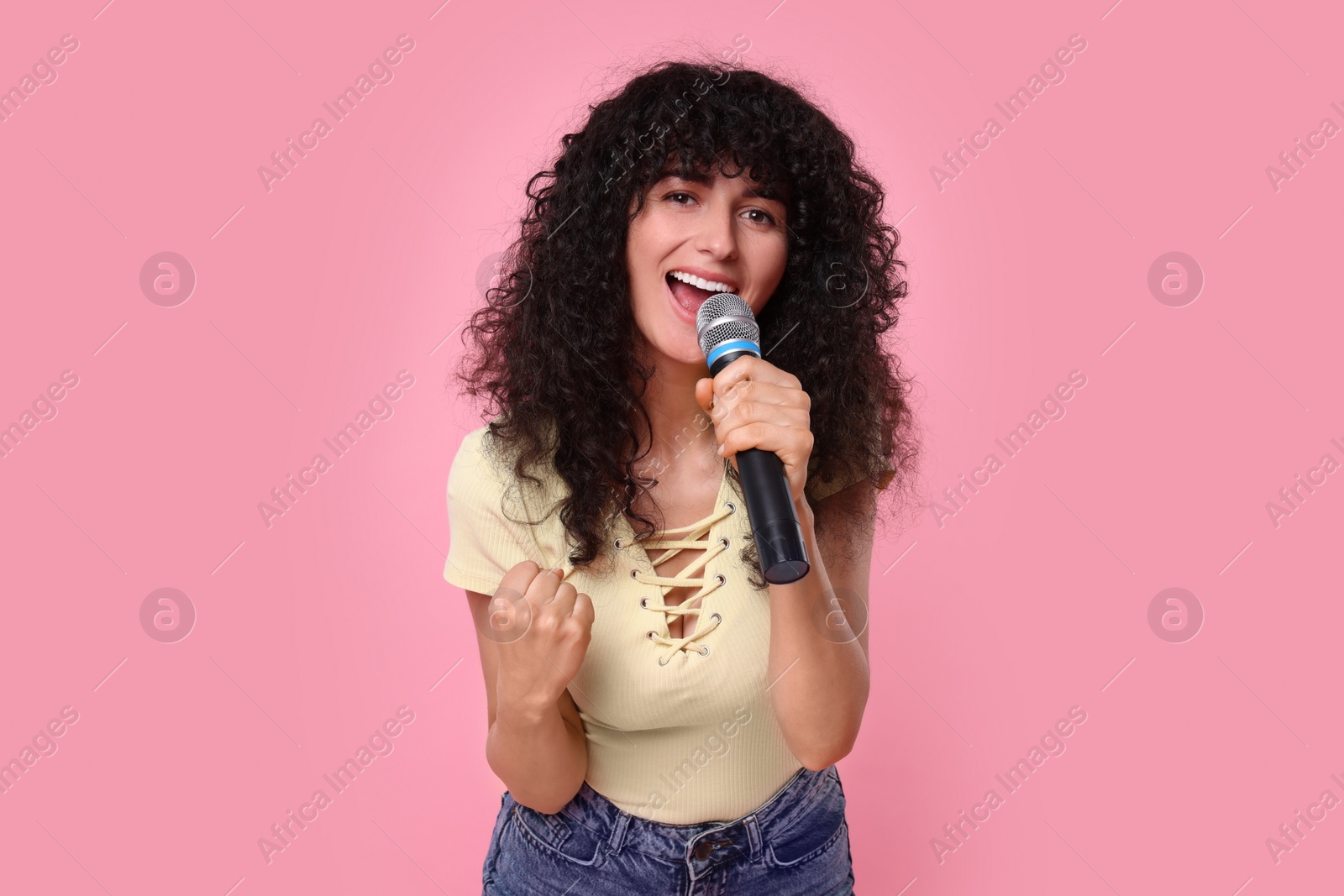 Photo of Beautiful young woman with microphone singing on pink background