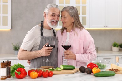 Happy affectionate senior couple with glasses of wine in kitchen
