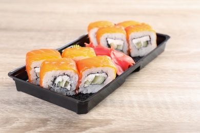 Box with tasty sushi rolls on wooden table. Food delivery