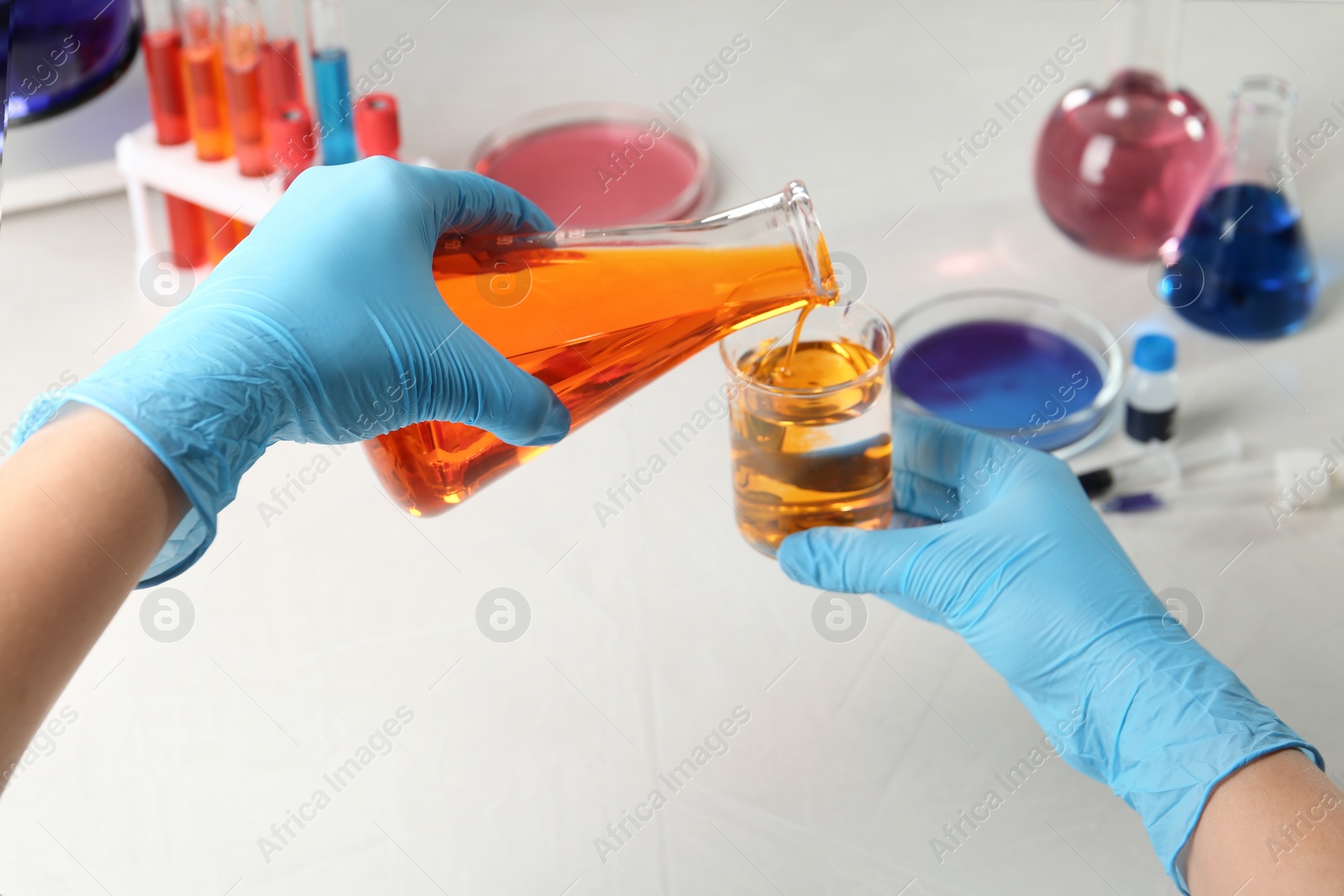 Photo of Scientist pouring reagent into beaker at table in chemistry laboratory, closeup