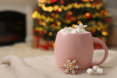 Photo of Christmas cocoa with marshmallows in pink cup on soft blanket indoors, closeup. Space for text