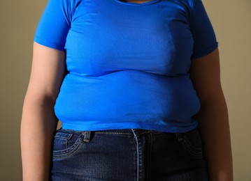 Photo of Overweight woman in tight t-shirt on light brown background, closeup