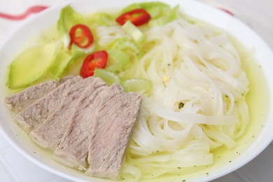 Photo of Bowl of delicious rice noodle soup with celery and meat on white table, closeup