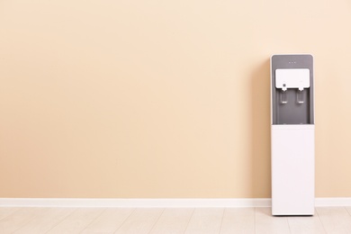 Photo of Modern water cooler against color wall with space for text