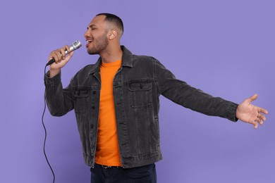 Photo of Handsome man with microphone singing on violet background