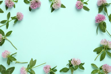 Photo of Frame of beautiful clover flowers on turquoise background, flat lay. Space for text