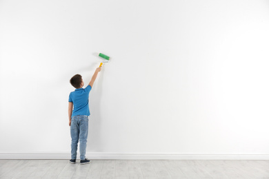 Photo of Little child painting with roller brush on white wall indoors. Space for text