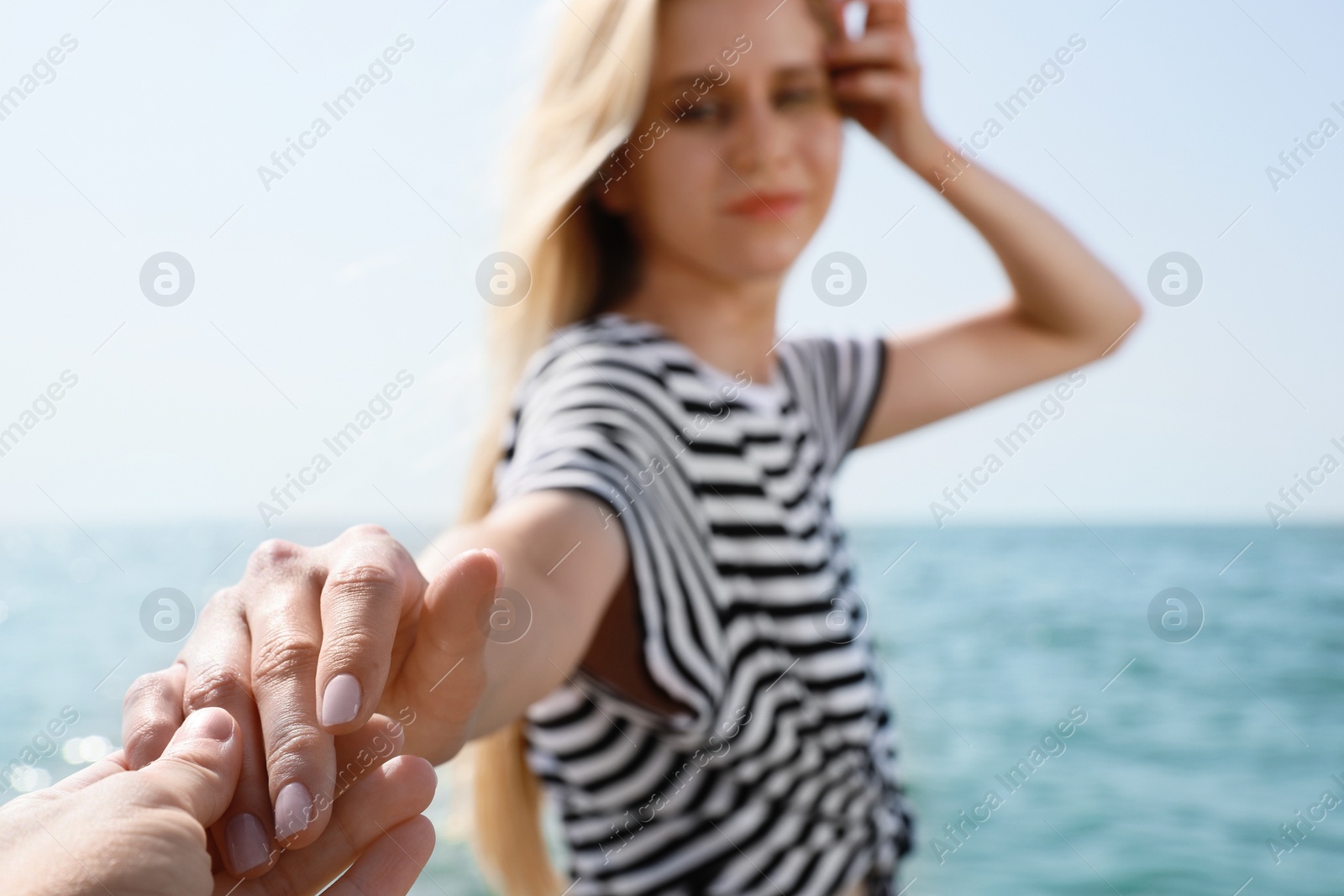 Photo of Young woman holding boyfriend's hand near sea on sunny day in summer