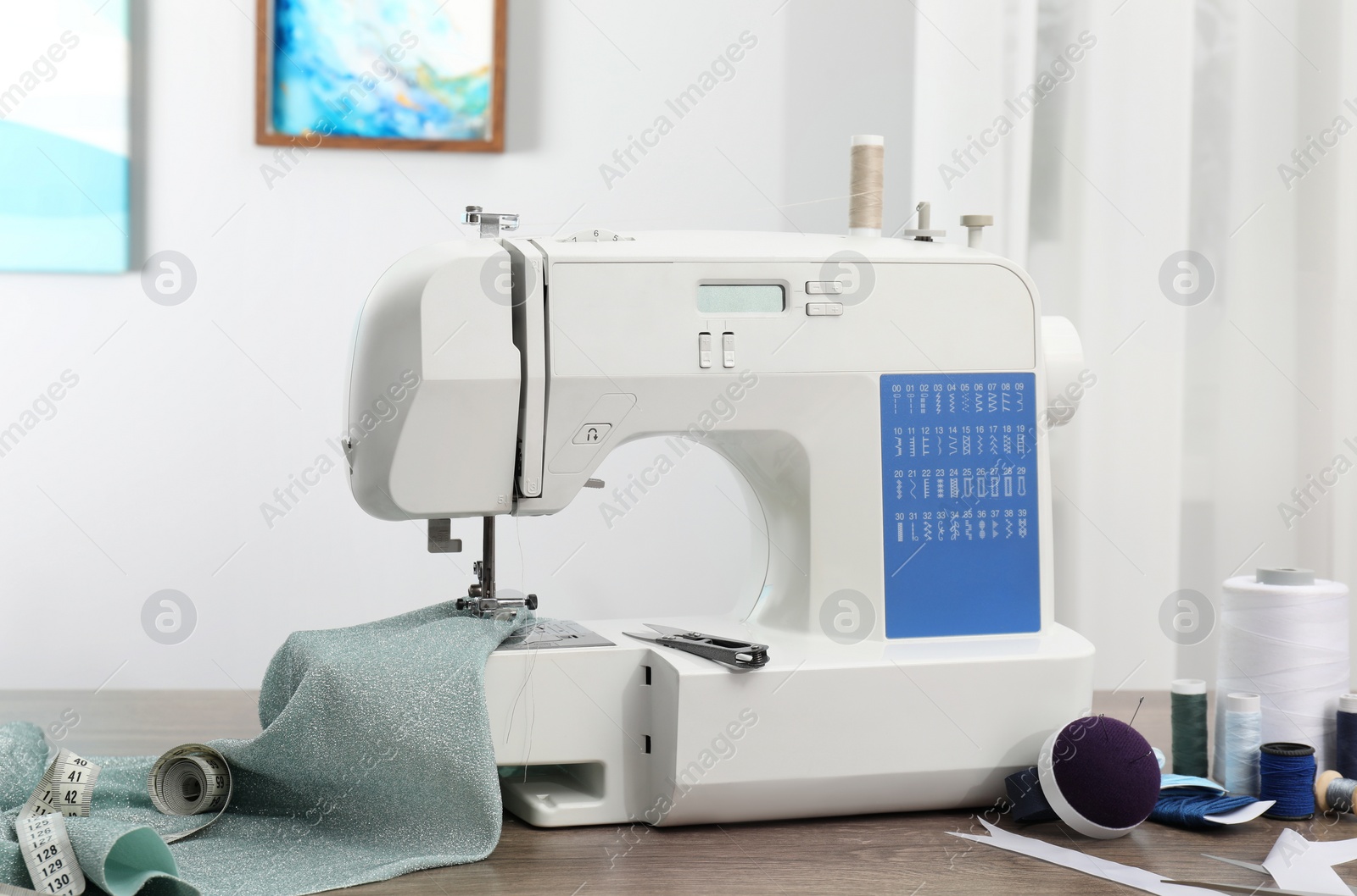 Photo of White sewing machine, cloth and craft accessories on wooden table indoors