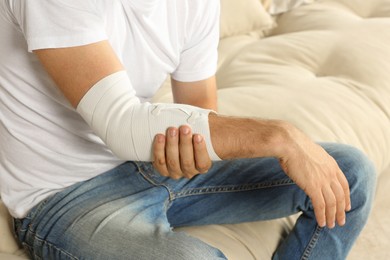 Photo of Man with arm wrapped in medical bandage on sofa, closeup