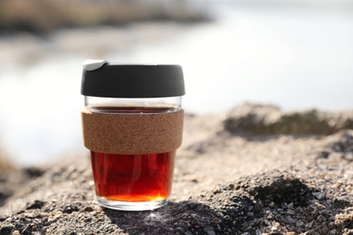 Photo of Reusable glass cup with hot drink on rock stone outdoors. Space for text