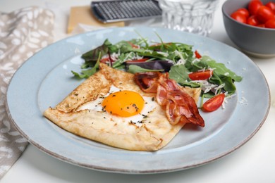 Photo of Delicious crepe with egg on white table. Breton galette