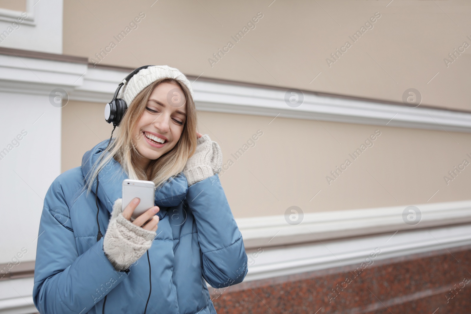 Photo of Young woman with headphones listening to music near light wall. Space for text