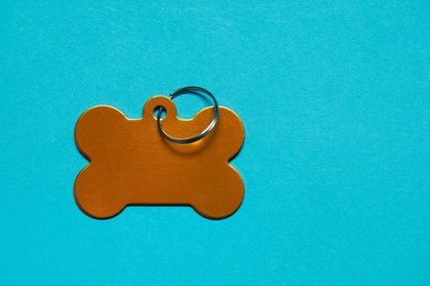 Photo of Golden pet tag in shape of bone with ring on yellow background, top view. Space for text