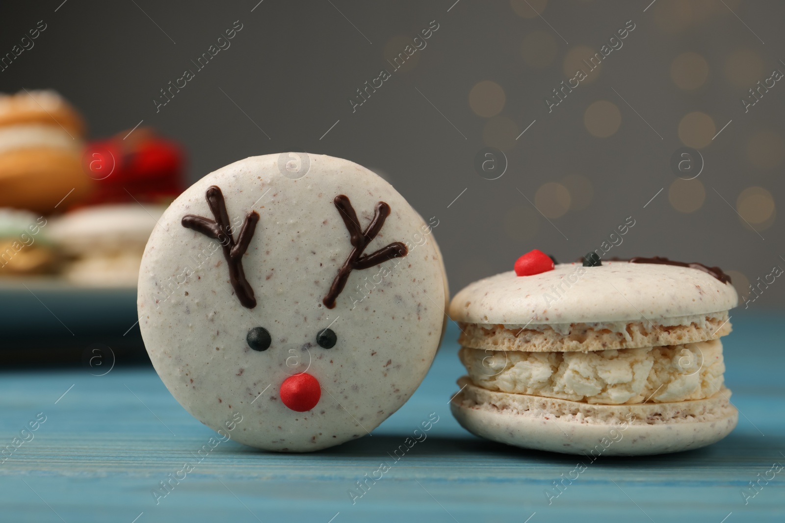Photo of Tasty reindeer Christmas macarons on light blue wooden table against blurred festive lights