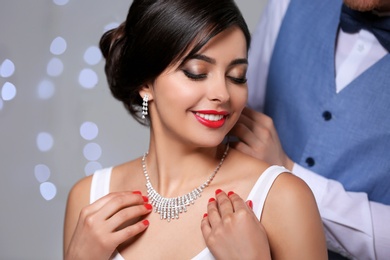 Photo of Man putting elegant jewelry on beautiful woman against blurred background