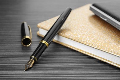 Photo of Stylish fountain pen and notebook on black wooden table, closeup