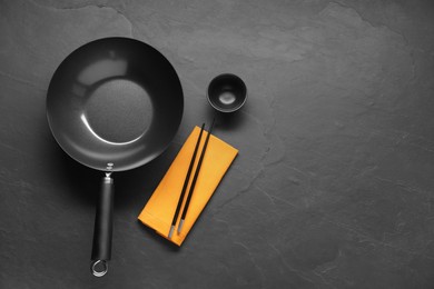 Empty iron wok, sauce bowl and chopsticks on black table, flat lay. Space for text