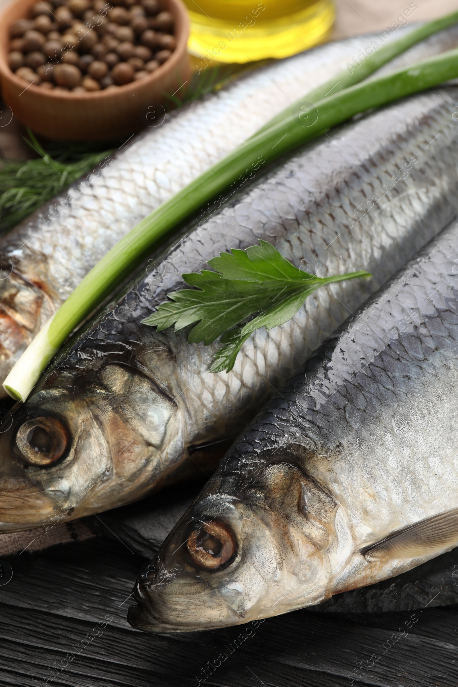 Photo of Delicious salted herrings and ingredients on black wooden table, closeup