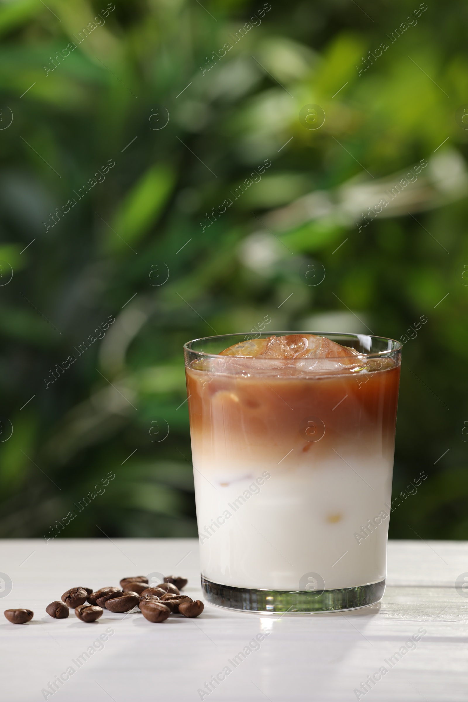 Photo of Glass of iced coffee and beans on white wooden table outdoors. Space for text