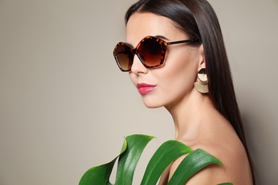 Beautiful woman in stylish sunglasses with tropical leaf on beige background. Space for text