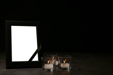 Photo of Empty frame with black ribbon and candles on table. Funeral symbol