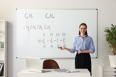 Photo of Young chemistry teacher giving lesson near whiteboard in classroom