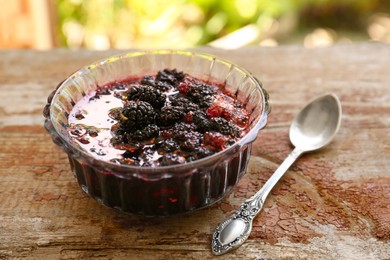 Photo of Bowl of sweet black mulberry jam and spoon on wooden table