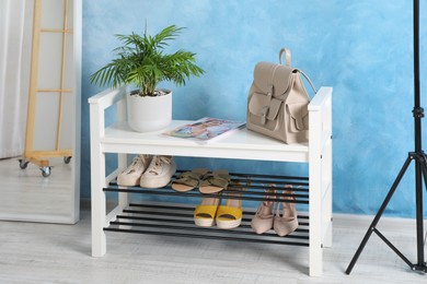 Photo of Shelving unit with stylish shoes and mirror near light blue wall in hall