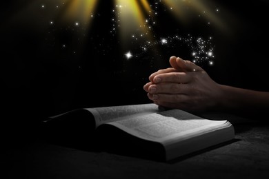 Christian woman praying over Bible under holy light in darkness, closeup