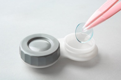 Photo of Tweezers with contact lens and container on light background, closeup