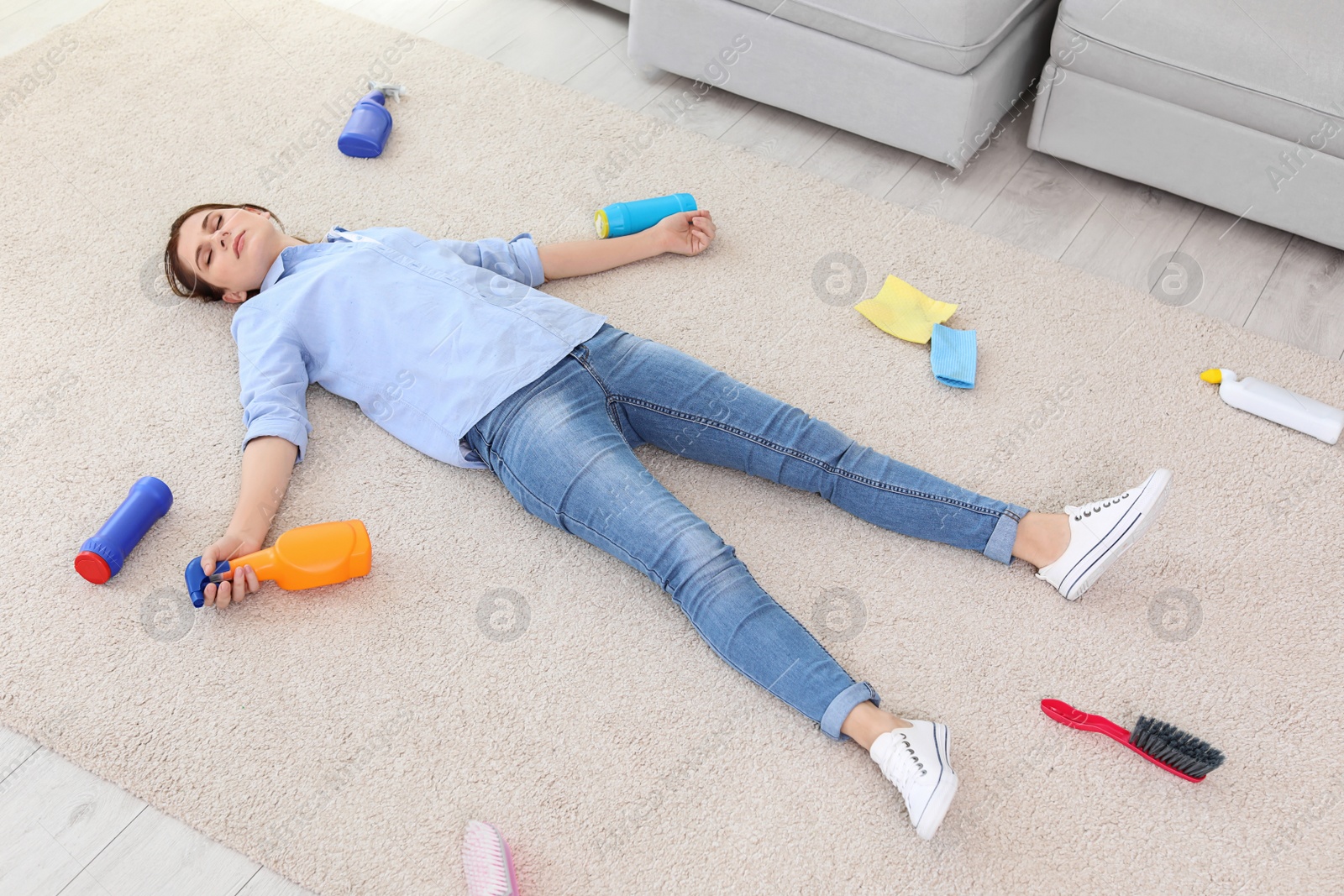 Photo of Tired woman lying on carpet surrounded by cleaning supplies