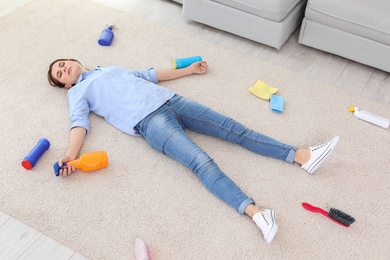 Tired woman lying on carpet surrounded by cleaning supplies