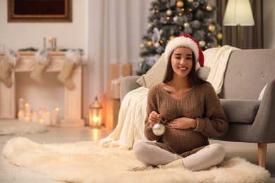 Happy pregnant woman with Christmas ball at home. Expecting baby