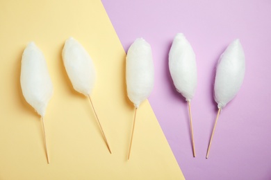 Sticks with yummy cotton candy on color background, top view