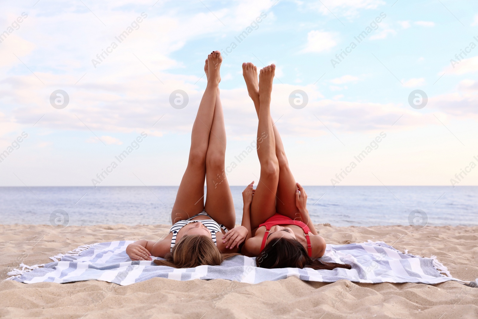 Photo of Young woman in bikini with girlfriend lying on beach mat. Lovely couple