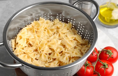 Cooked pasta in metal colander and tomatoes on grey table, closeup