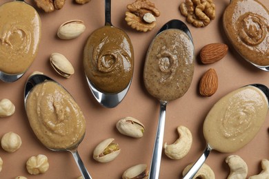 Tasty nut butters in spoons and raw nuts on light brown table, flat lay