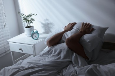 Photo of Sleepy man covering head with pillow in bed at home