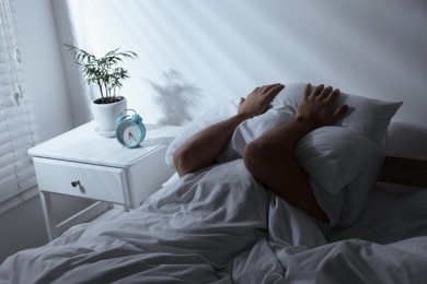 Sleepy man covering head with pillow in bed at home