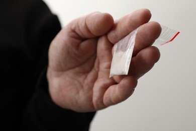 Photo of Drug addiction. Man with plastic bag of cocaine on light background, closeup