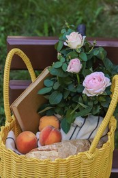 Yellow wicker bag with roses, book and peaches on wooden bench outdoors, closeup